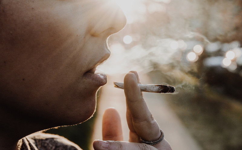 A woman smoking a joint breathing in cannabis smoke.